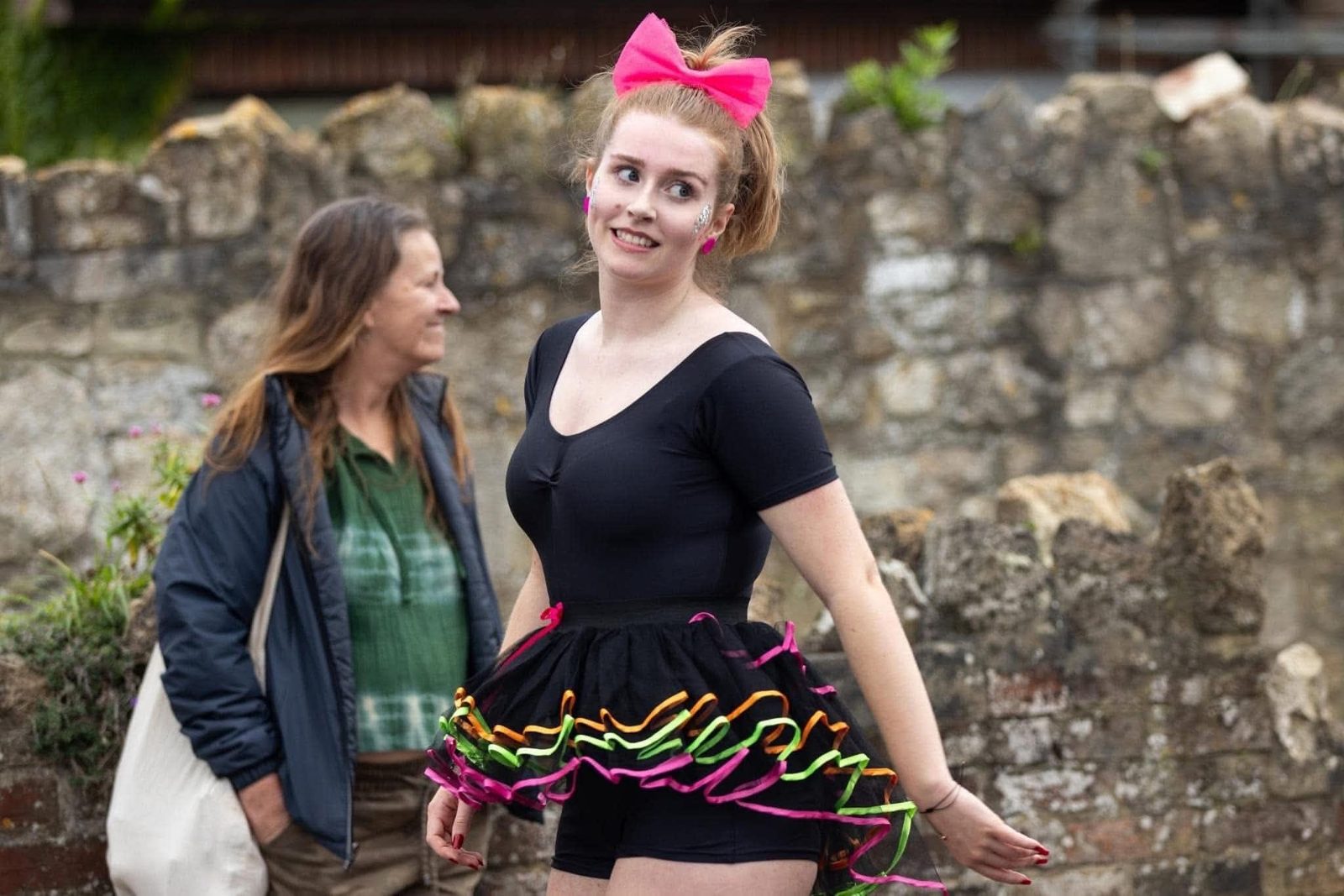 A performer in a black leotard, neon-trimmed tutu and pink hair bow dancing in a street carnival parade