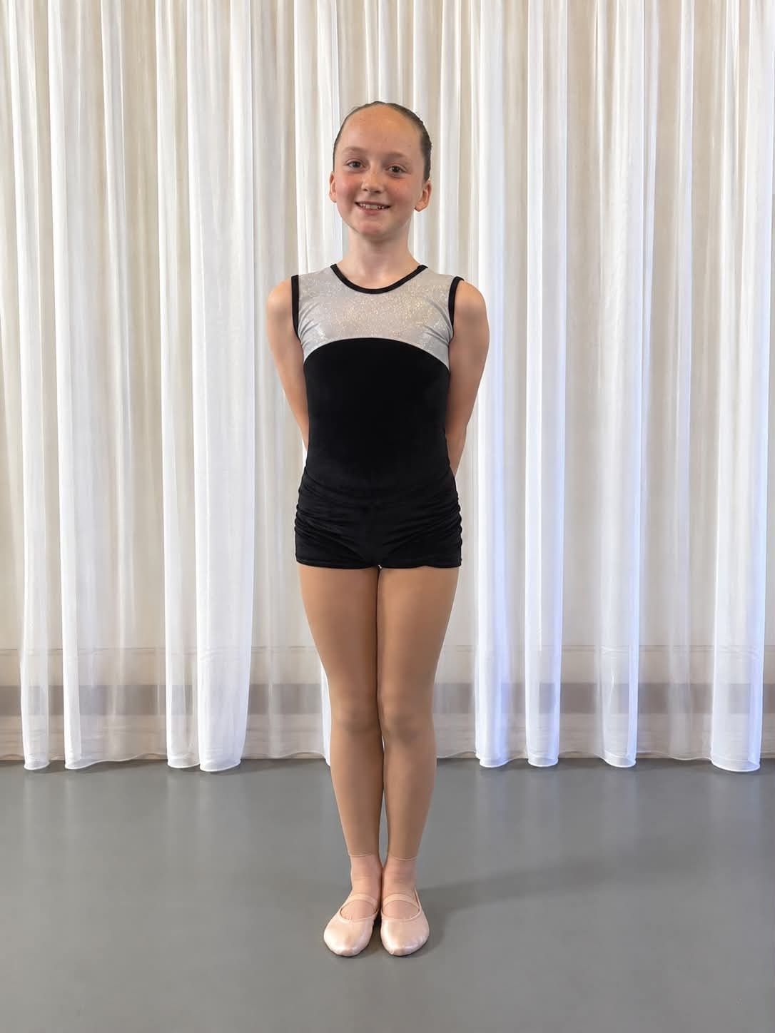 A student in a black and silver sparkle leotard with black shorts and pink ballet shoes