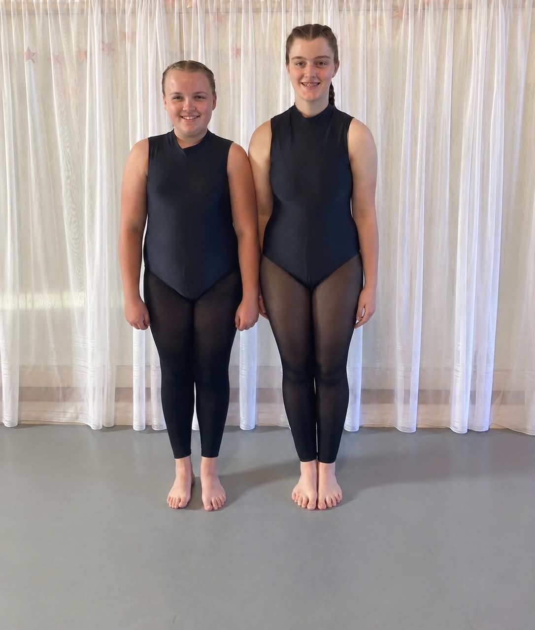 Two upper school students in black high-neck leotards and sheer black tights, standing barefoot