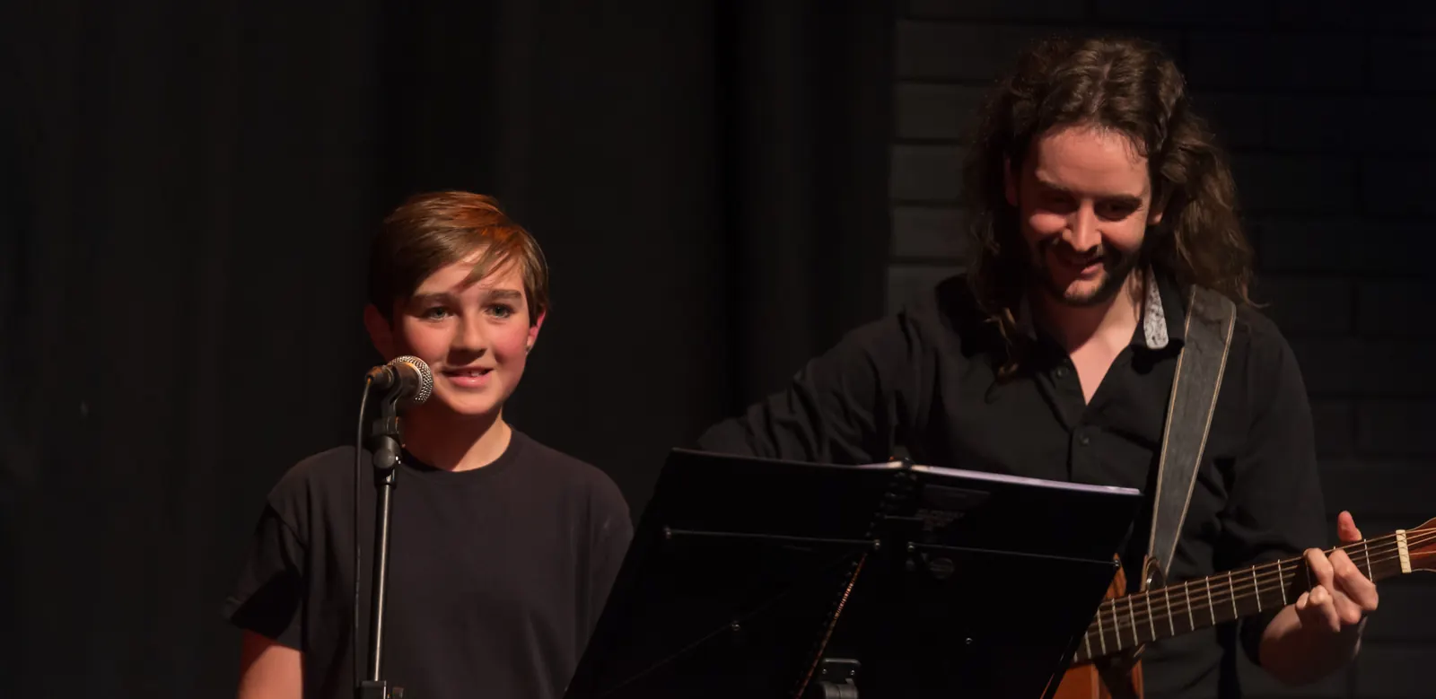 Mr Mike playing guitar beside a young ESSOPA student singing into a microphone