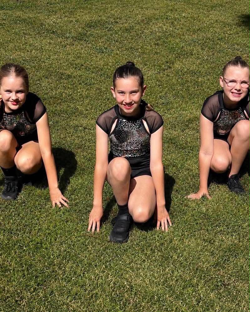 Three ESSOPA students in matching black performance costumes crouching on the grass outdoors